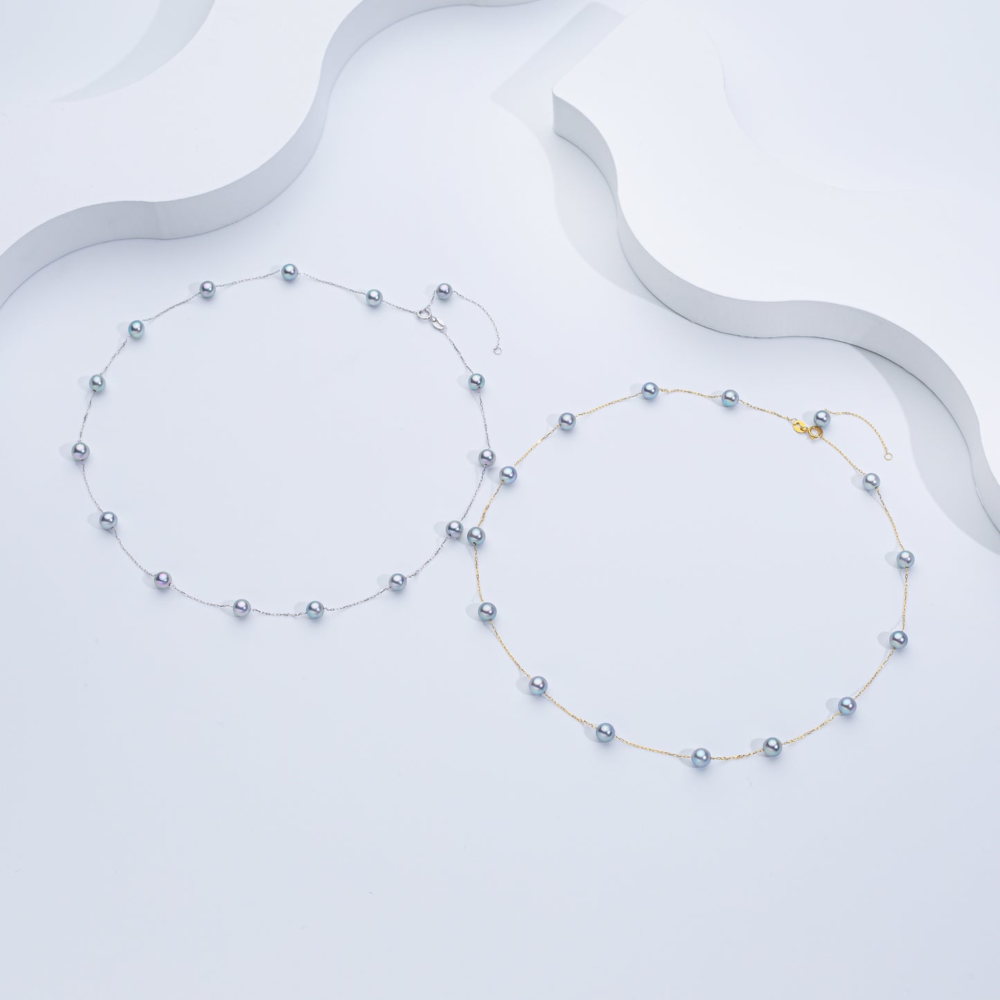 Two Akoya Sea Pearl necklaces, one with the pearls strung on a gold chain and another with the pearls in a silver-tone setting, displayed against a white background.