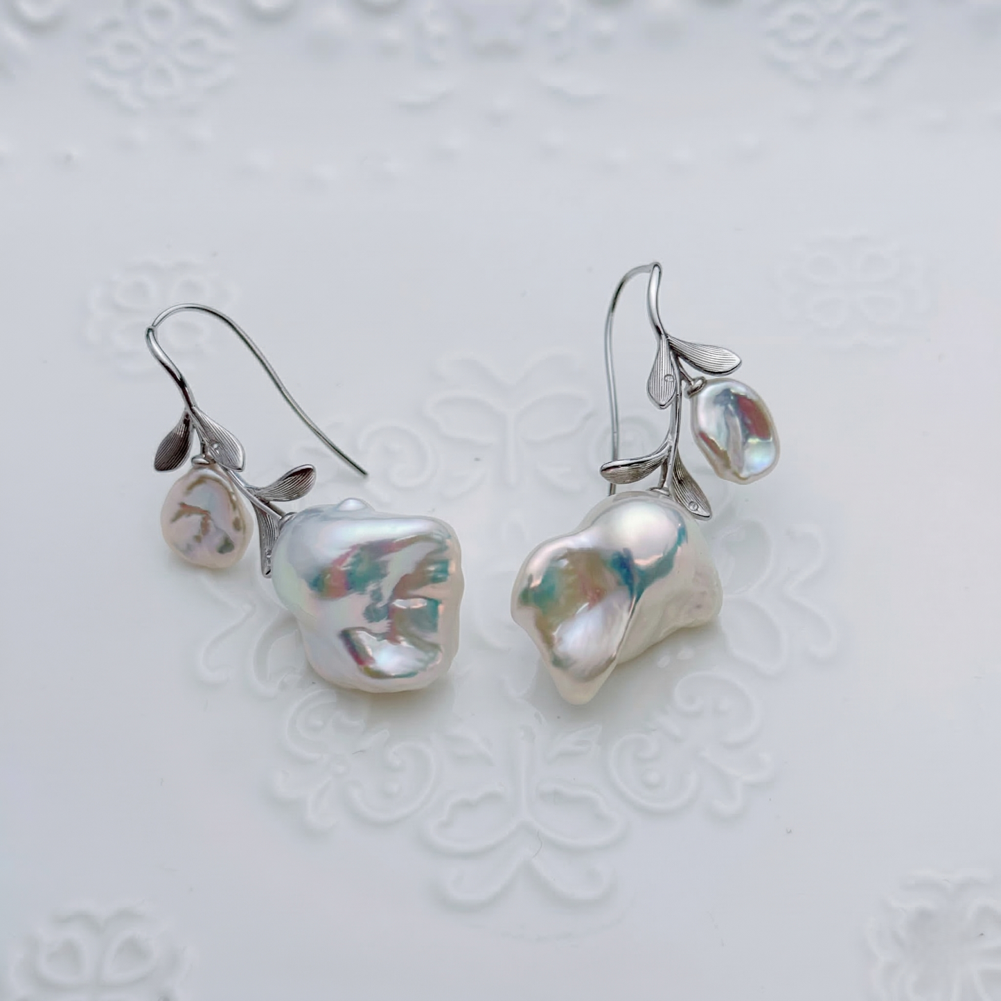 Pearl earrings with silver leaves on a textured white background