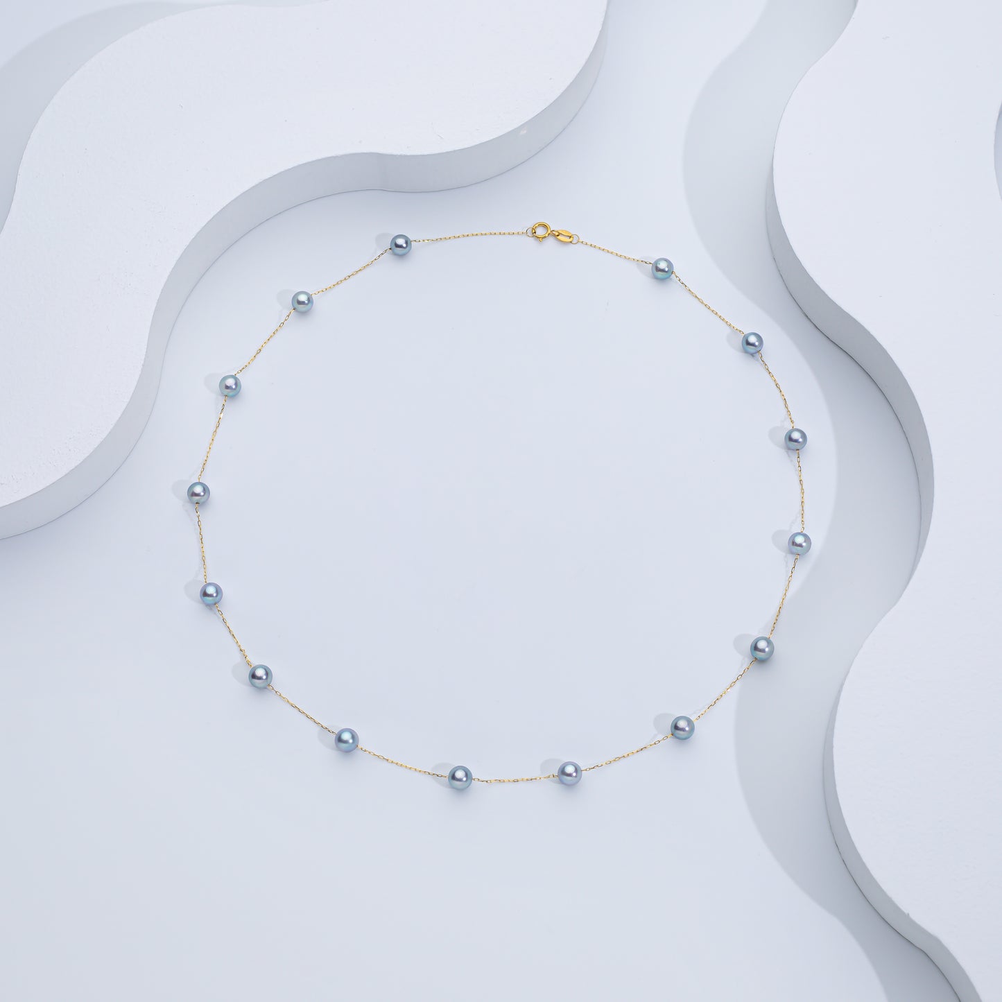 A silver Akoya sea pearl necklace displayed on a white, wave-shaped surface.