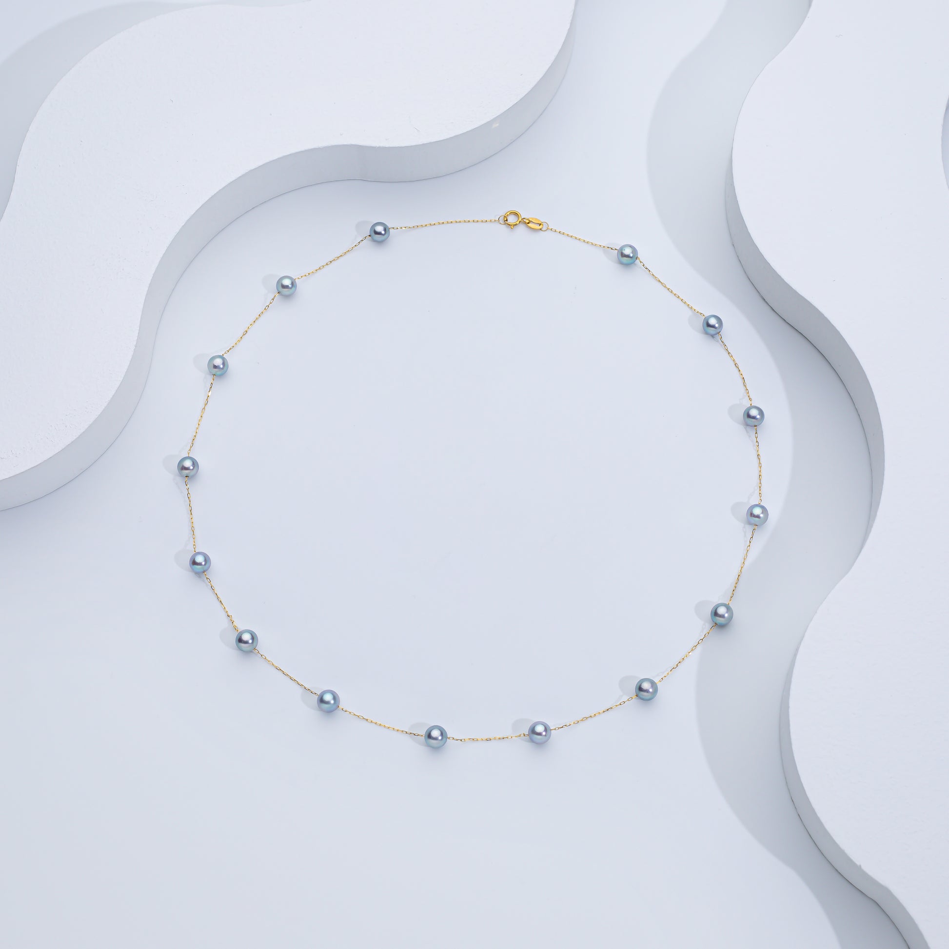 A silver Akoya sea pearl necklace displayed on a white, wave-shaped surface.